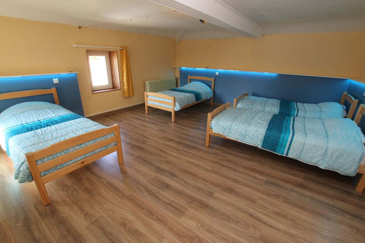 Ein Zimmer mit drei hölzernen Betten, jeweils mit einer blau-weißen Bettdecke. Der Raum verfügt über Holzböden und ein Fenster mit einem gelben Vorhang.