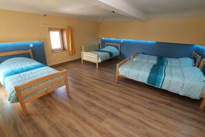Ein Zimmer mit drei hölzernen Betten, jeweils mit einer blau-weißen Bettdecke. Der Raum verfügt über Holzböden und ein Fenster mit einem gelben Vorhang.