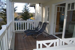 Eine überdachte Veranda mit zwei Loungestühlen, einem weißen Geländer und einer Glastür zum Innenbereich.