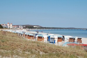 Ein Strand mit mehreren Reihen von Strandkörben und einem Steg, der ins Meer führt.