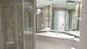 Casa de banho moderna com chuveiro de vidro, um espelho grande e bancada de granito.