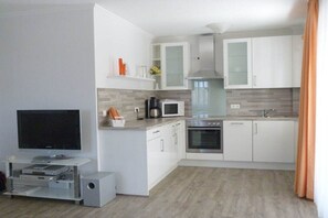 Eine moderne Küche mit weißen Schränken, einer Mikrowelle, einem Backofen und einem integrierten Fernseher.