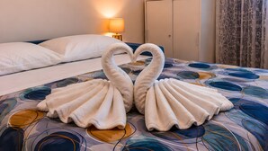 Een bed met een decoratieve handdoekdecoratie in de vorm van twee zwanen, een nachtkastje met een lamp en een wandklok.