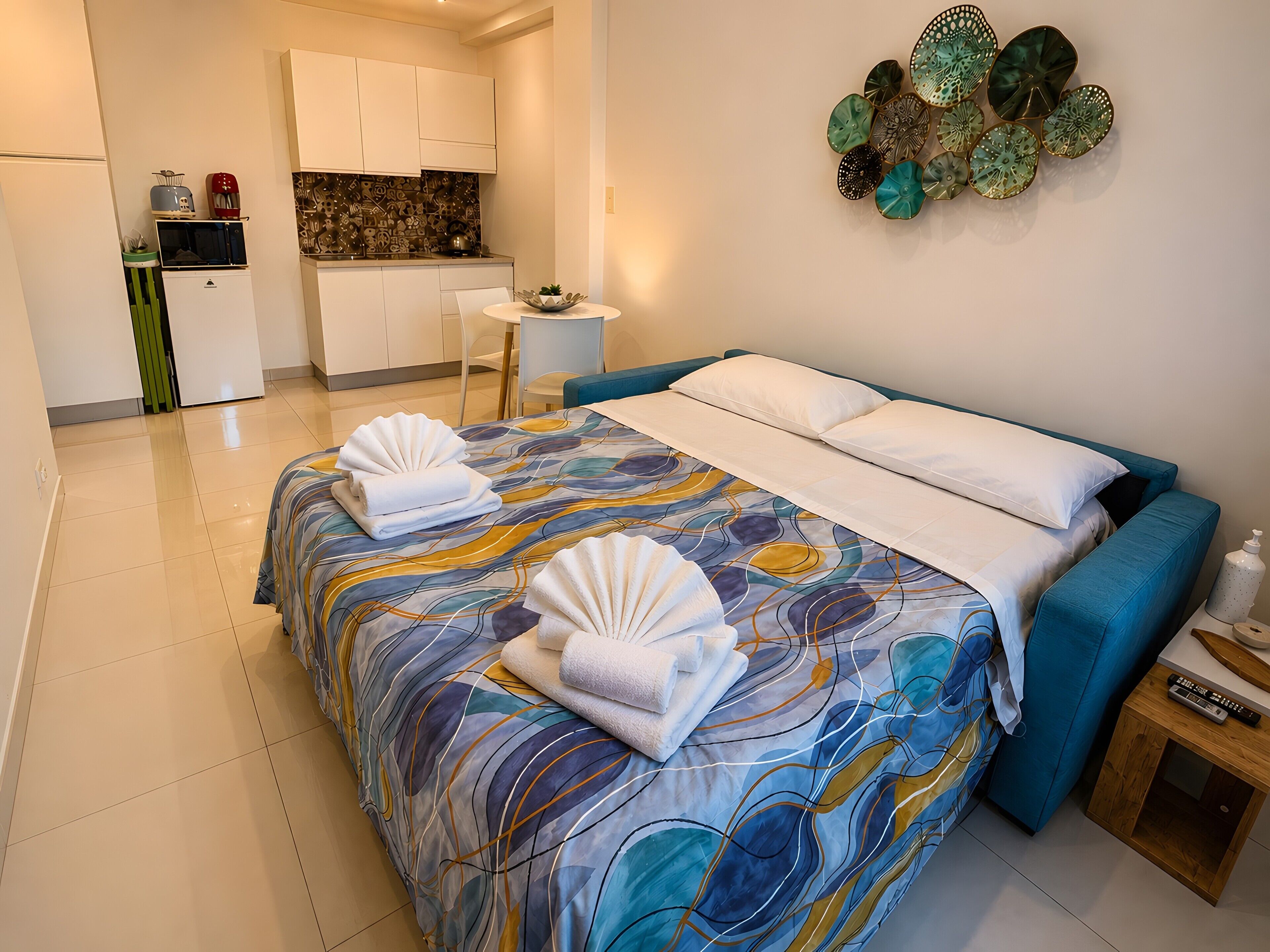 Une chambre d’hôtel avec un lit, une petite table, une chaise et, au fond, un coin cuisine.