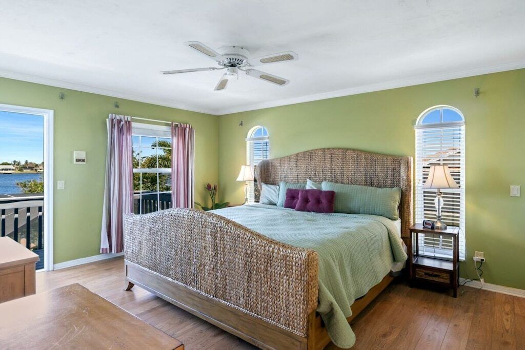 Ein Schlafzimmer mit einem großen Bett, einem Deckenventilator, einem Nachttisch mit Lampe und Meerblick durch ein Fenster.