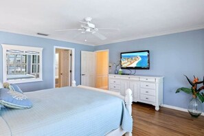 Ein Schlafzimmer mit einem Bett, einem Fernseher, einer weißen Kommode und einem Deckenventilator.