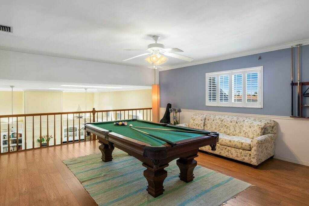 A pool table in a room with a ceiling fan, a sofa, and a window with blinds.