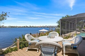 Eine Terrasse mit Korbmöbeln und einem Pool, mit Blick auf ein Gewässer.