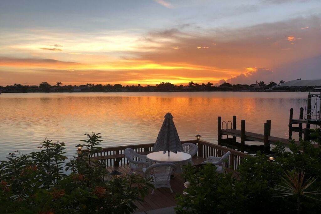 A waterfront patio with a table and chairs, overlooking a calm lake during sunset.