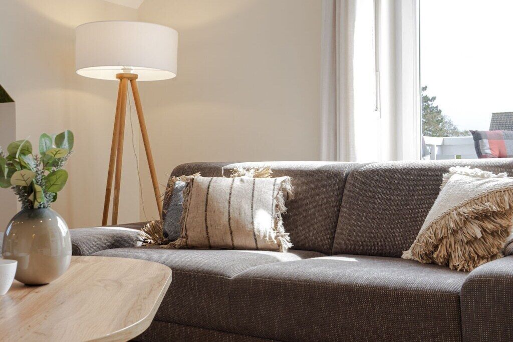 A living room with a sofa, a lamp, and a vase with plants.