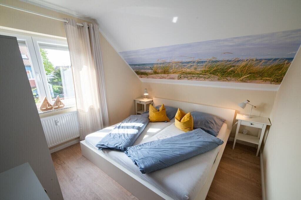 A bedroom with a bed, a nightstand, a window with curtains, and a beach mural on the wall.