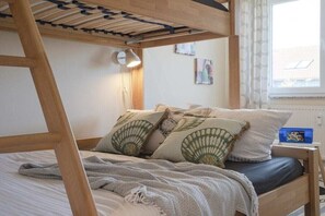 Ein Schlafzimmer mit Etagenbett, Nachttisch mit Lampe und einem Fenster mit Vorhängen.