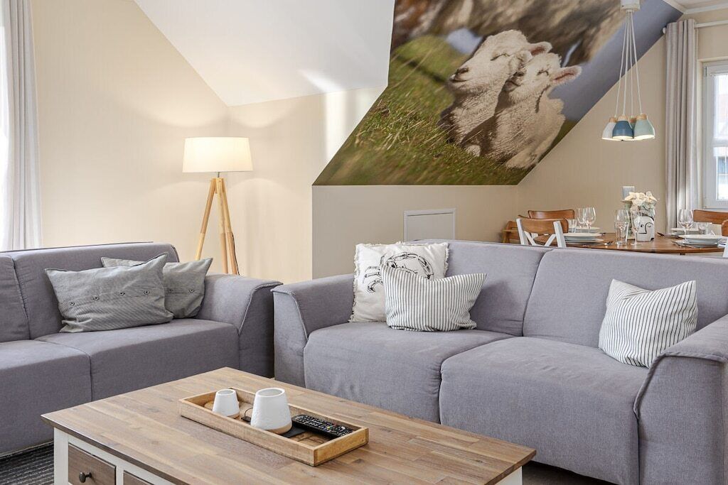 A modern living room with a grey sofa, a wooden coffee table, and a painting of sheep on the wall.