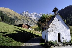 A white church with a steep roof and a bell tower, surrounded by a rural landscape with a mountain backdrop. - Holiday home with 1 bedroom (Obermaiselstein)