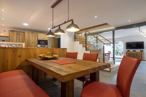 A modern kitchen with wooden cabinets, a dining table with red chairs, and a staircase leading to an upper level. - Holiday home with 1 bedroom (Obermaiselstein)