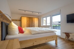 A bedroom with a wooden bed, a wardrobe, a television, and a window with a view. - Holiday home with 1 bedroom (Obermaiselstein)