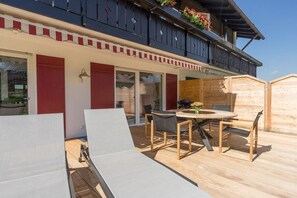 A wooden deck with a table and chairs, a sliding glass door, and a red-framed window. - Holiday home with 1 bedroom (Obermaiselstein)