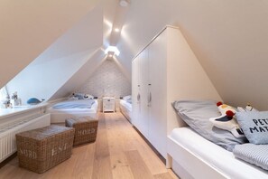 Ein Schlafzimmer mit schrägem Dach, einem Bett, einer Kommode und einem Fenster.