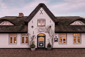 Ein traditionelles, weißes Gebäude mit einem Reetdach, einem zentralen Rundbogenportal und symmetrischen Fenstern.