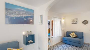 Un salon avec un canapé, un mur d’accent bleu, un tableau représentant un paysage côtier et un sol carrelé.