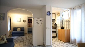 Espaço compacto com sofá, geladeira, cozinha e mesa de jantar. A cozinha possui um painel de azulejos.