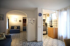 Un espace de vie compact comprenant un canapé, un réfrigérateur, un coin cuisine avec un dosseret carrelé et une table à manger.