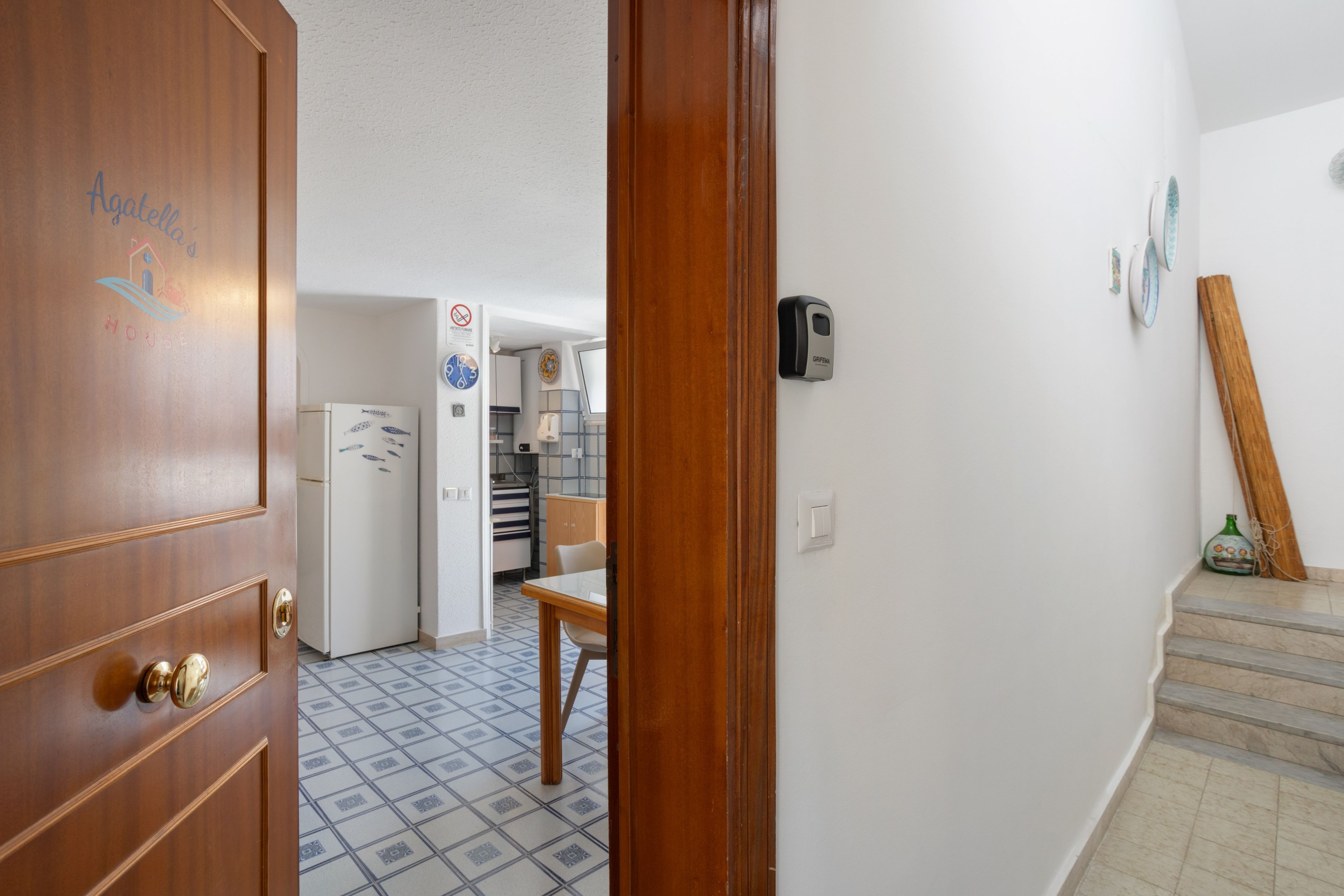 Una porta in legno con una maniglia, un pavimento piastrellato, un angolo cottura con frigorifero e un tavolo da pranzo.