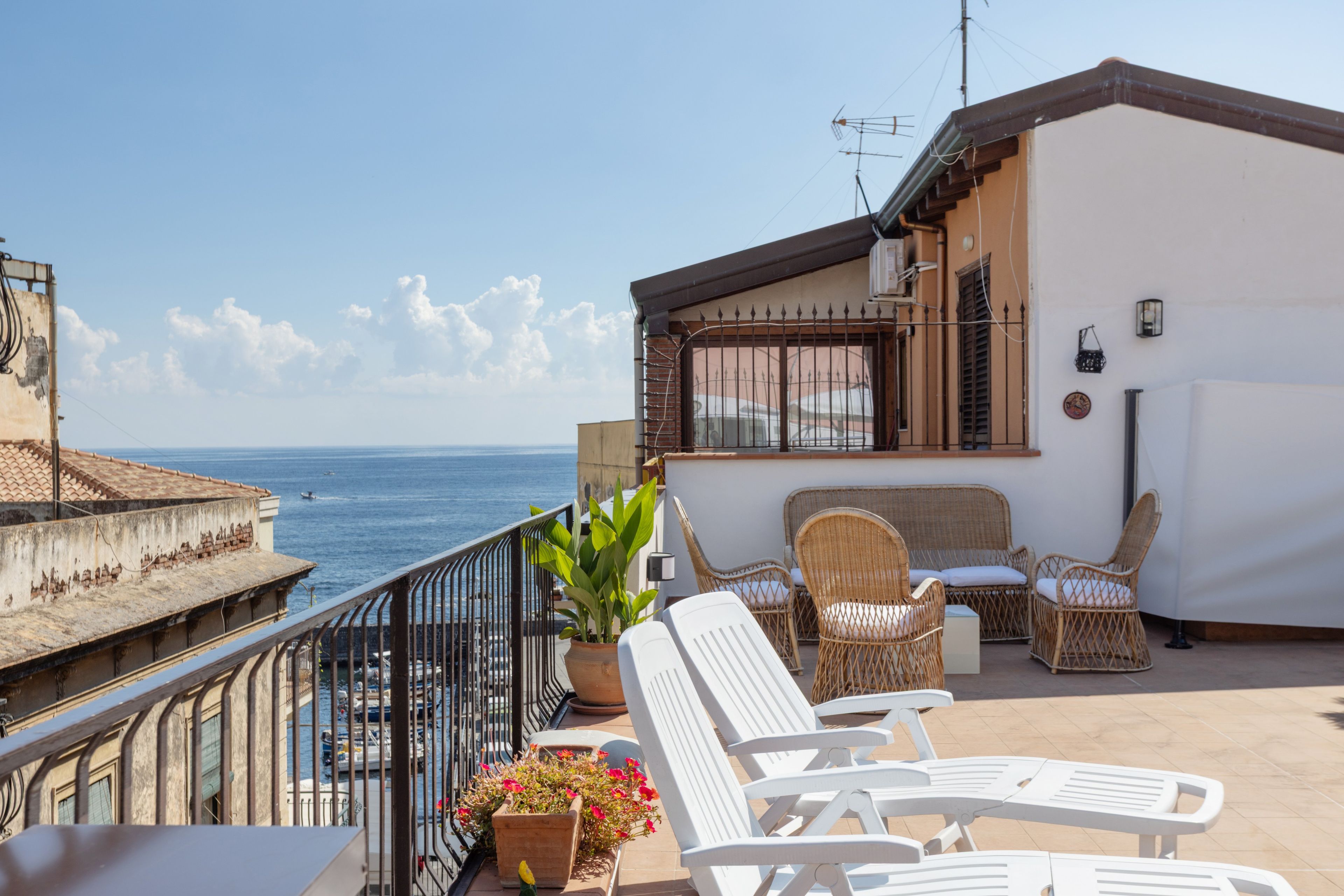 Eine Terrasse mit Blick auf das Meer, Korbmöbel und Kübelpflanzen.
