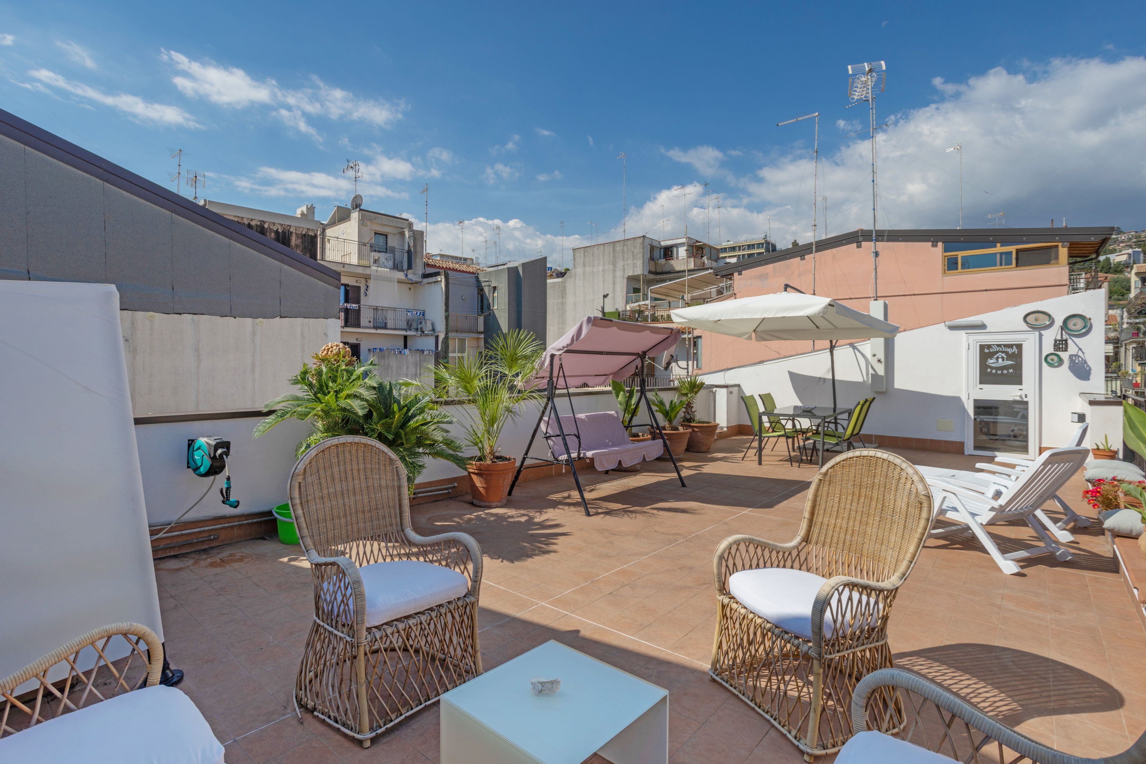 A rooftop terrace with wicker furniture, potted plants, and a swing.