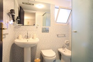 Une salle de bain avec un lavabo, deux toilettes, un miroir et une fenêtre.
