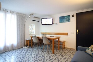 A small, tidy room with a dining table, chairs, a television, a window with curtains, and a door.