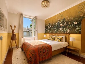 A bedroom with a bed, a window, a painting, a lamp, and a wooden floor. - Le Vernet – Avignon City Center – Air-Conditioned (Avignon)