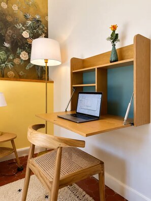 A workspace with a laptop on a wooden shelf, a chair, a lamp, and a wall with a floral painting. - Le Vernet – Avignon City Center – Air-Conditioned (Avignon)