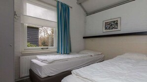 Une chambre avec deux lits, une fenêtre avec un rideau, un radiateur et un tableau encadré au mur.