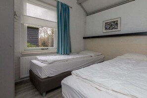 Ein Zimmer mit zwei Betten, einem Fenster mit Vorhang, einem Heizkörper und einem gerahmten Bild an der Wand.