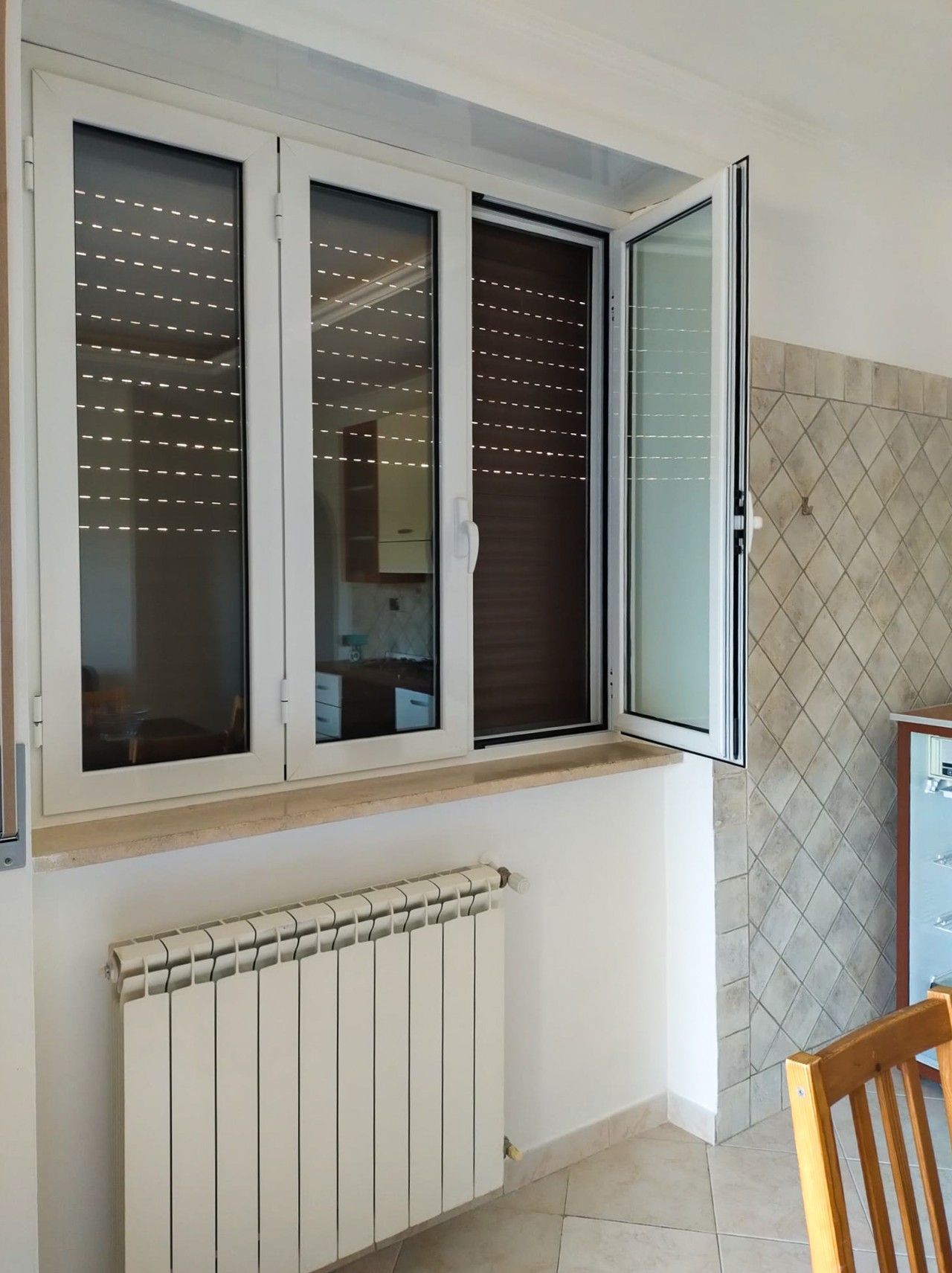 Ein Zimmer mit Fenster, Heizkörper und gefliesten Wänden.