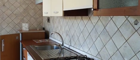 Una cocina con estufa a gas, un lavamanos y alacenas.