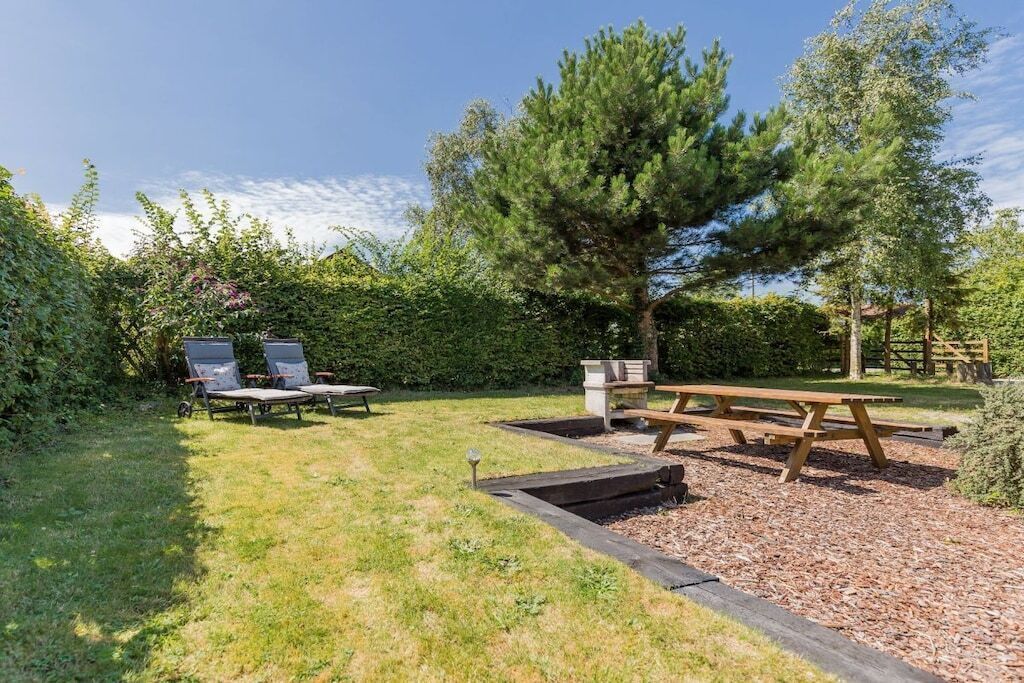 Un jardin avec une table de pique-nique en bois, deux chaises longues et un grand arbre.