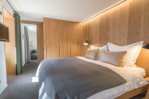 A modern bedroom with a wooden headboard, a large bed with white bedding, a bedside lamp, and a view into a bathroom. - Holiday apartment with 1 bedroom (Oberstdorf)
