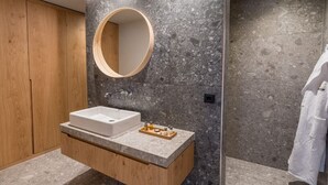 Un bany modern amb un lavabo independent, un tocador de fusta, un mirall rodó i un assecador de tovalloles.