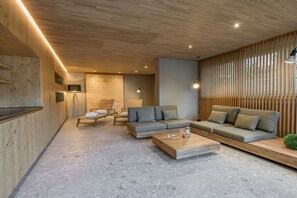 A modern interior with a wooden ceiling, a grey sofa, a coffee table, and a wooden wall with vertical slats. - Holiday apartment with 1 bedroom (Oberstdorf)