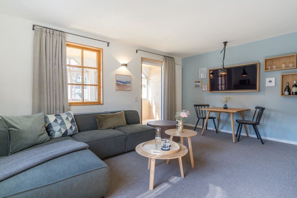 Een moderne woonkamer met een hoekbank, een eethoek met tafel en stoelen, en een groot raam met gordijnen.