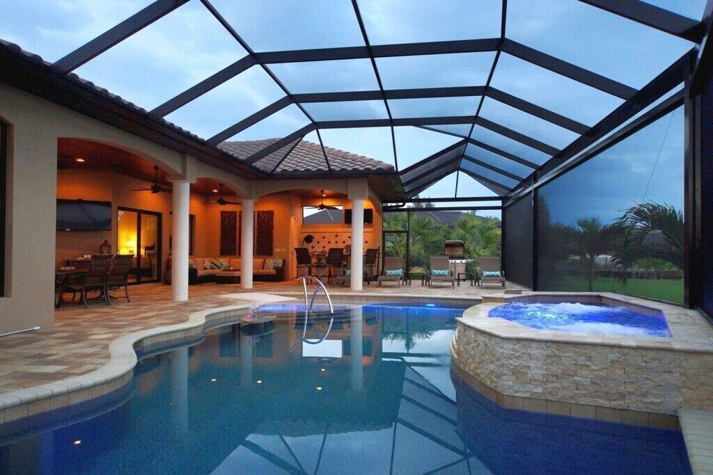 An indoor swimming pool with a glass ceiling, a hot tub, and a patio area with outdoor seating.