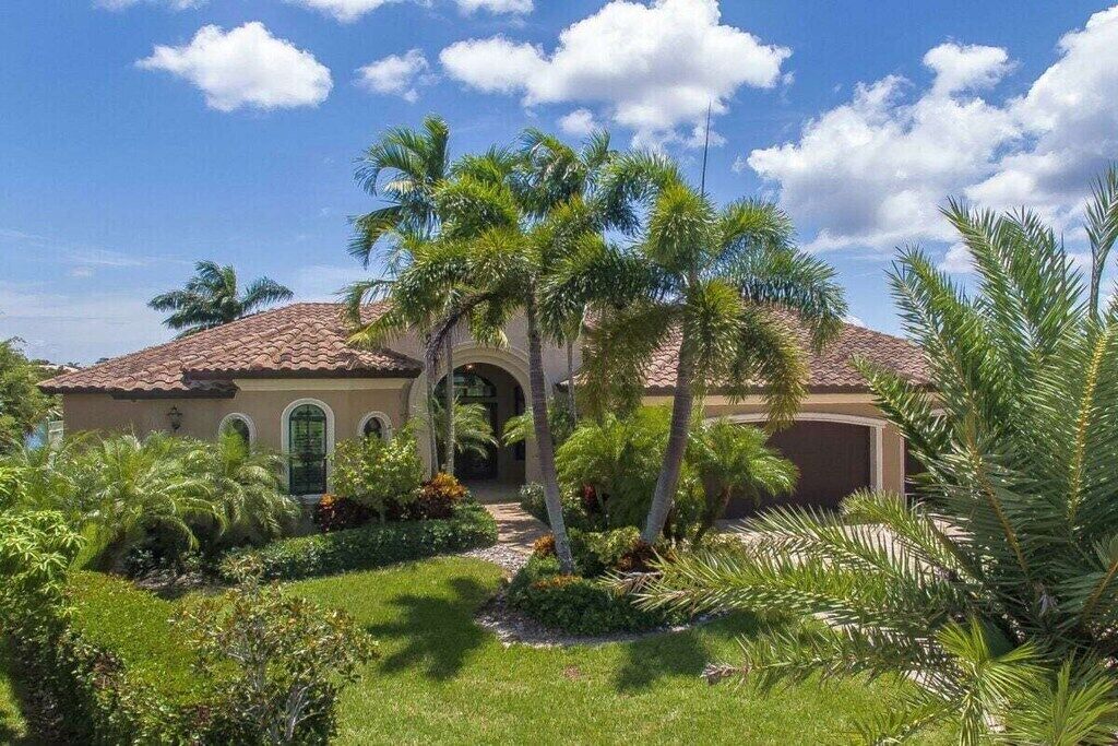 A house with a tiled roof, arched windows, and a well-maintained garden with palm trees.