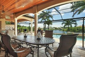 An outdoor patio with a round table and chairs, a pool, and a view of palm trees and hills. - CCVS - Villa Ambience 5* (Cape Coral)