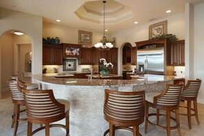 A spacious kitchen with a large island, bar stools, and modern appliances. - CCVS - Villa Ambience 5* (Cape Coral)