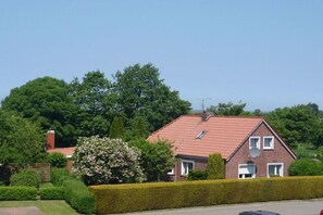 A residential house with a red-tiled roof, surrounded by greenery and a well-maintained hedge. - Holiday apartment with 1 bedroom (Dornumersiel)
