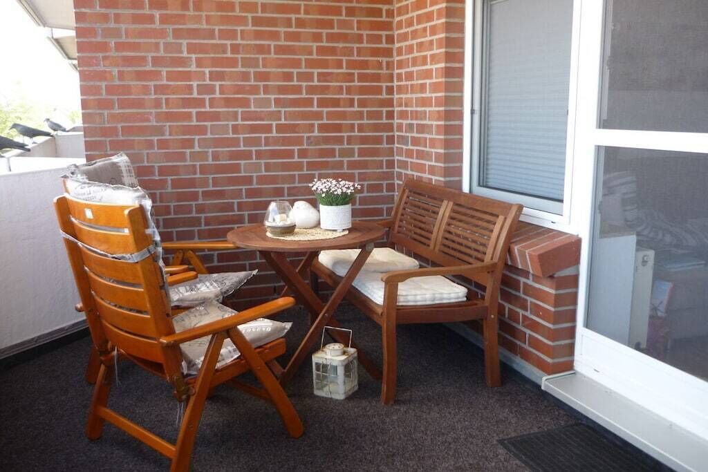 Un coin terrasse avec un mur en briques, une table ronde, deux chaises en bois et une petite lanterne.