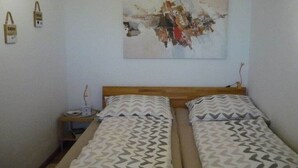 Quarto com duas camas, cabeceira de madeira, mesa de cabeceira e uma pintura abstrata na parede.