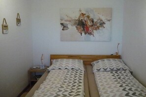 A room with two beds, a wooden headboard, a nightstand, and a wall-mounted abstract painting. - Holiday apartment with 1 bedroom (Dornumersiel)